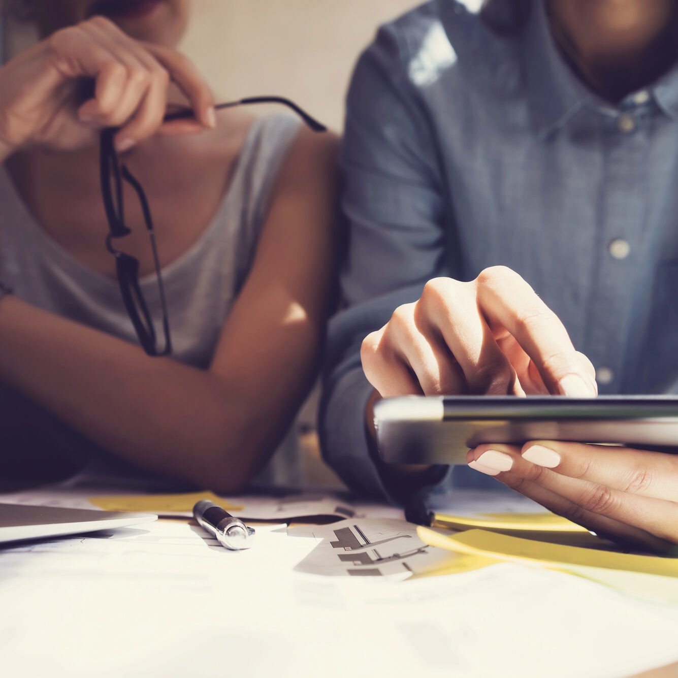 Two people sitting at a desk while one of them uses a tablet to fill in information, suggesting a step in creating an online account.
